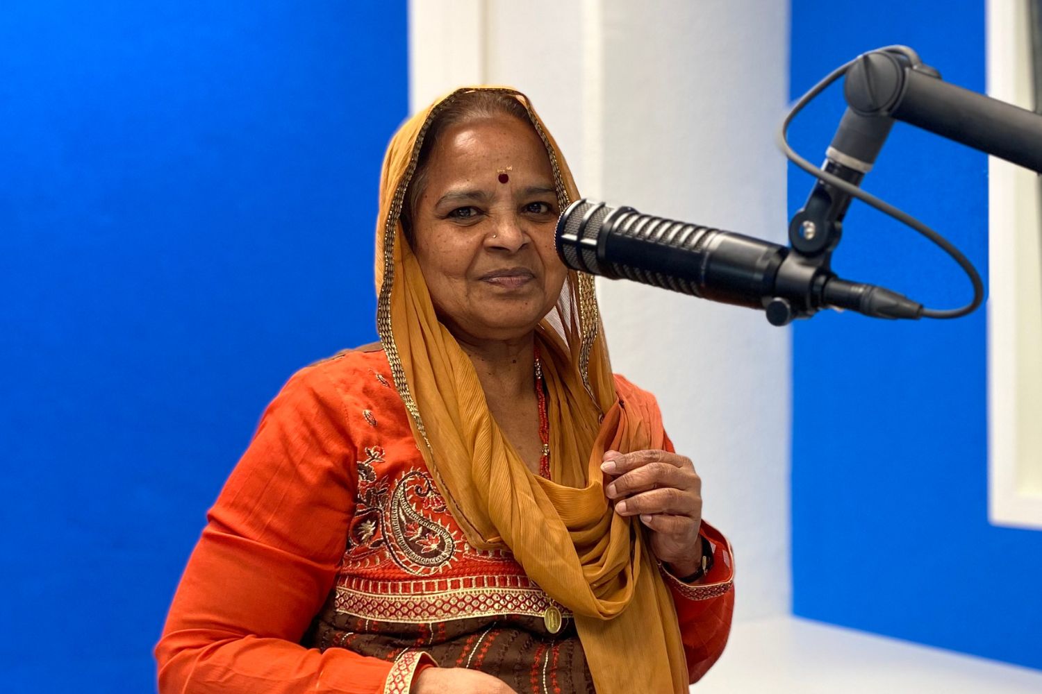 Nirmala in front of a microphone in special clothing for Diwali Festival. Host of Bhakti Margam.