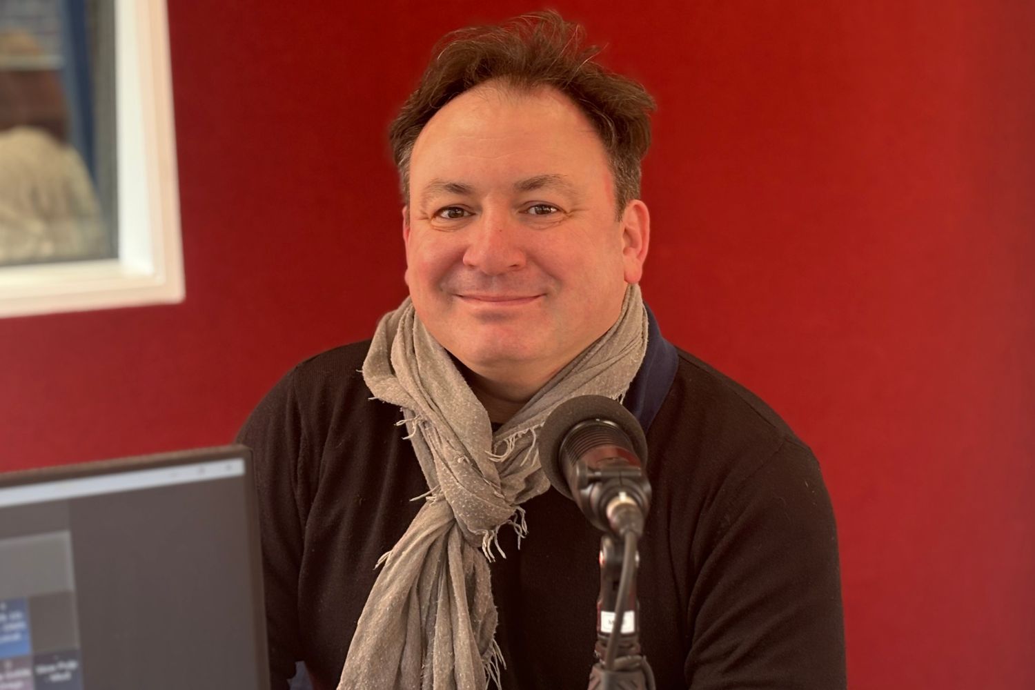 A photo of Duncan Connors in the OAR FM studio in front of a red wall