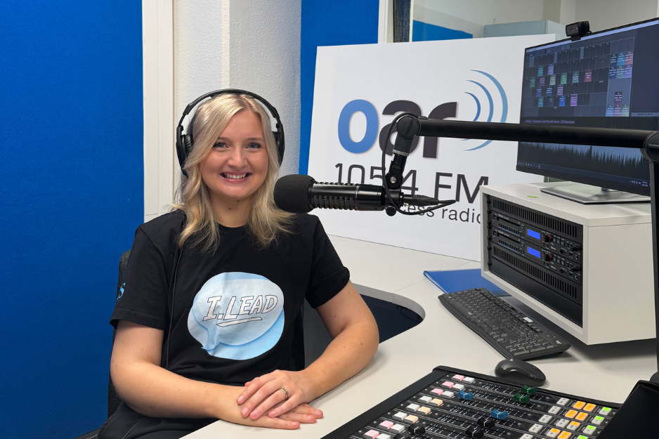 Hannah Butson, host of the I.Lead Podcast smiles infront of a microphone in the OAR FM studios.