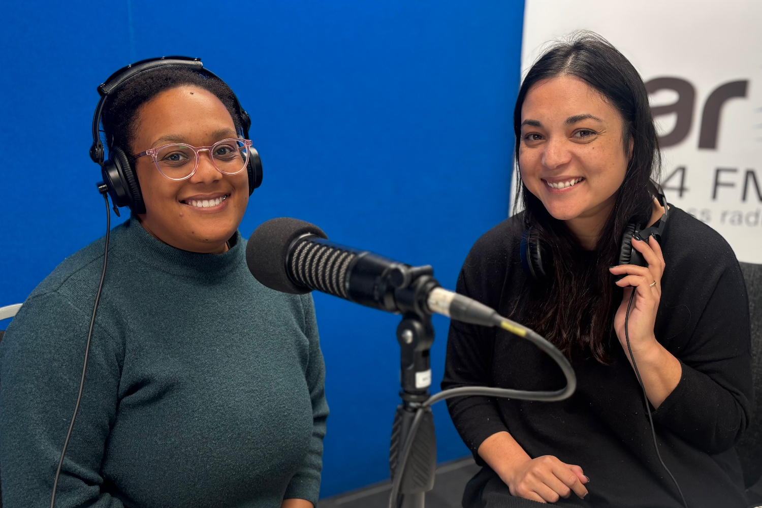 Photo of Cori and Colette in the OAR FM Studio. Cori is in front of a microphone and Colette has headphones around her neck.