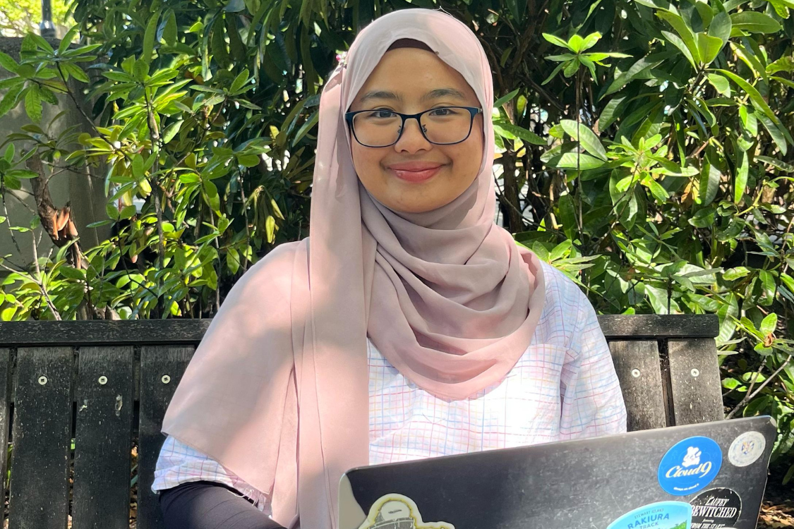 Host of Sofea Study Space, Sofea Haizal sits on a bench in the park with a laptop on her lap