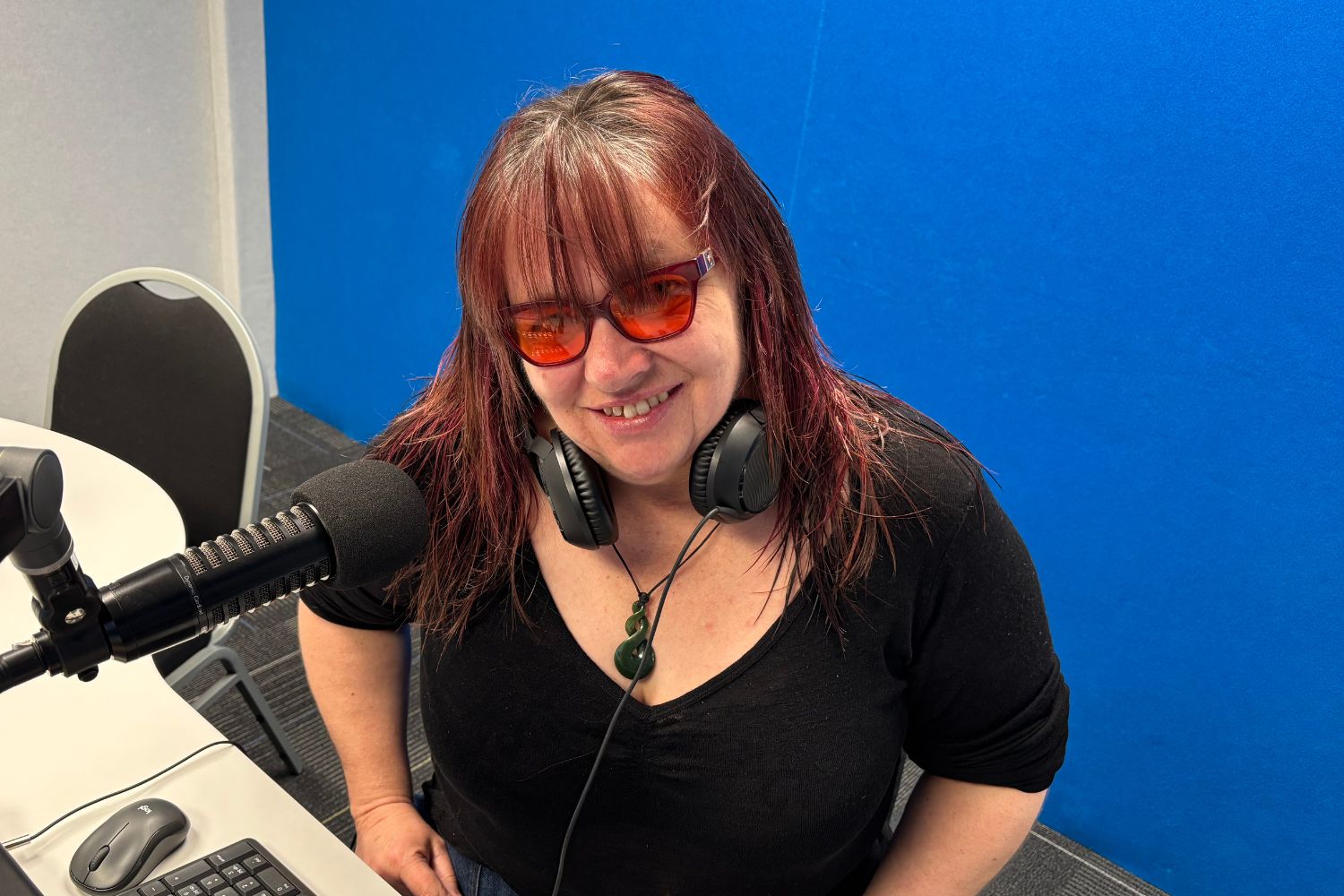 Photo of host Leeann Barnett in recording studio next to a microphone and in front of a blue wall